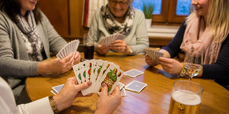 Drei Frauen sitzen an einem runden Tisch und spielen Karten, Nahaufnahme der Hände mit Spielkarten